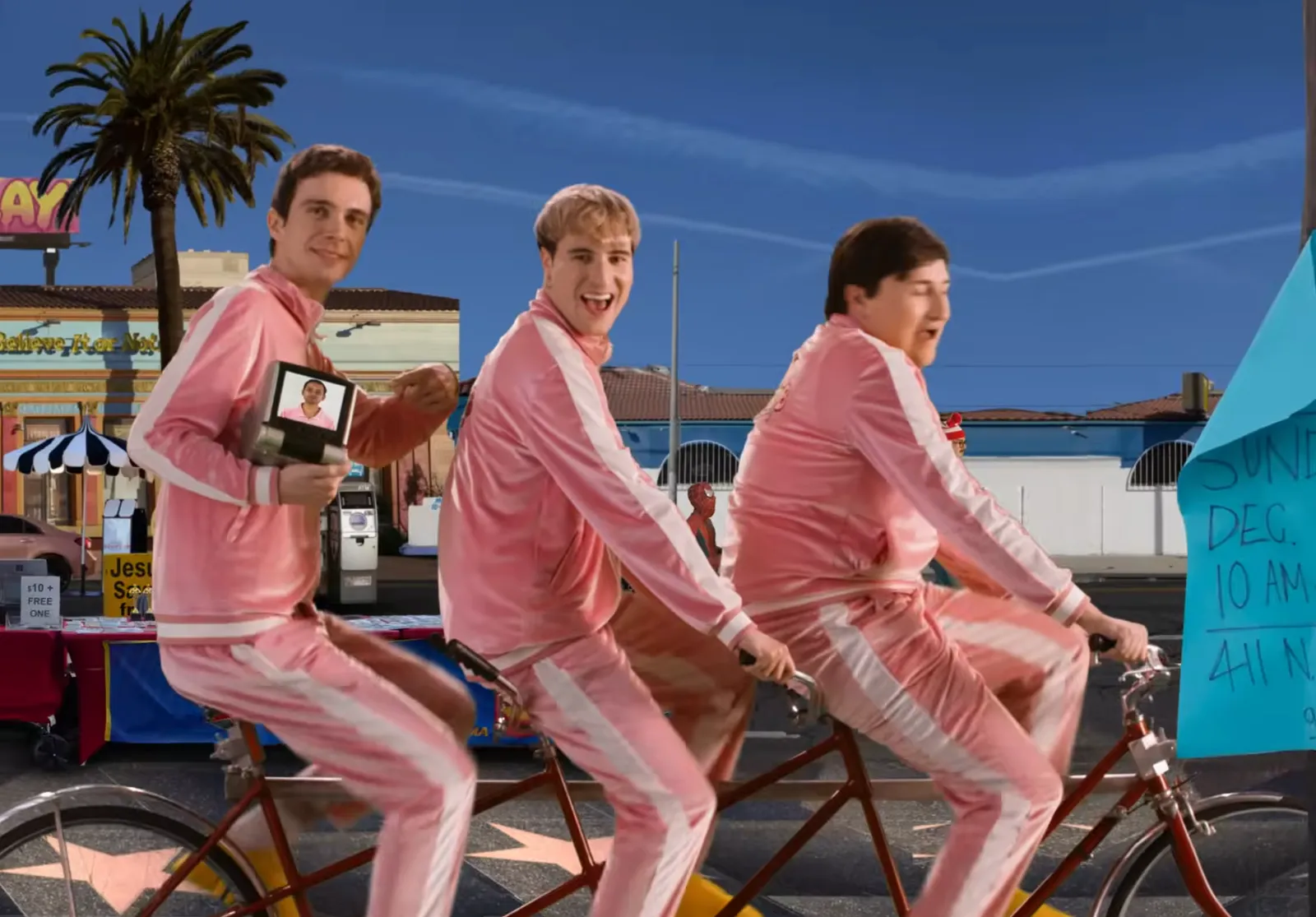 Boy Throb writing a tandem bicycle with the fourth member, Darshan, on a telepromper to join them remotely.